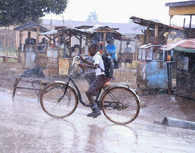 Oeganda - Kampala - jongen met fiets door de regen.